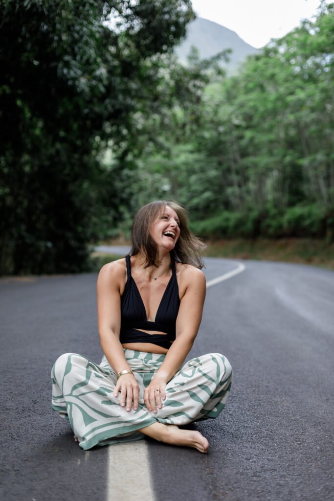 portrait d'une femme assise sur la route en tailleur en train de rire elle est heureuse photo prise par marie production photographe basée à rennes en bretagne