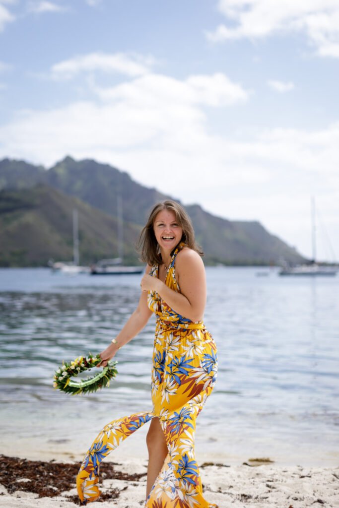 photo femme en robe d'été jaune avec une couronne de fleurs à la main au bord du lagon à moorea en polynesie française prise par marie production photographe située à rennes en bretagne